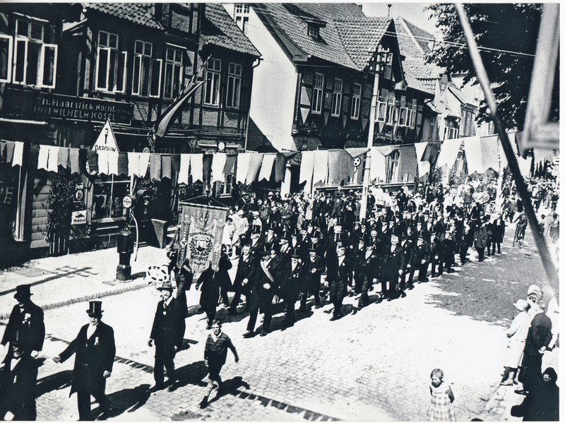 Foto 5 - Schützenumzug in der Marktstraße. Links vor dem Haus des Kaufmanns Kosel (heute Drogeriemarkt Rossmann) die erste Tankstelle für Kraftfahrzeuge 1927